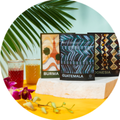 A colorful assortment of bags of tea from Burma, Guatemala, and Indonesia, with cups of tea and green in the background.