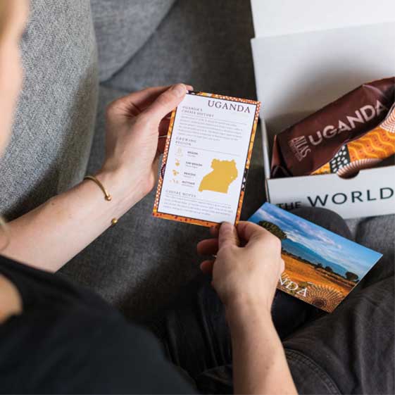 A person opening their box of Atlas Tea on their couch, reading a card with country info and tasting notes.